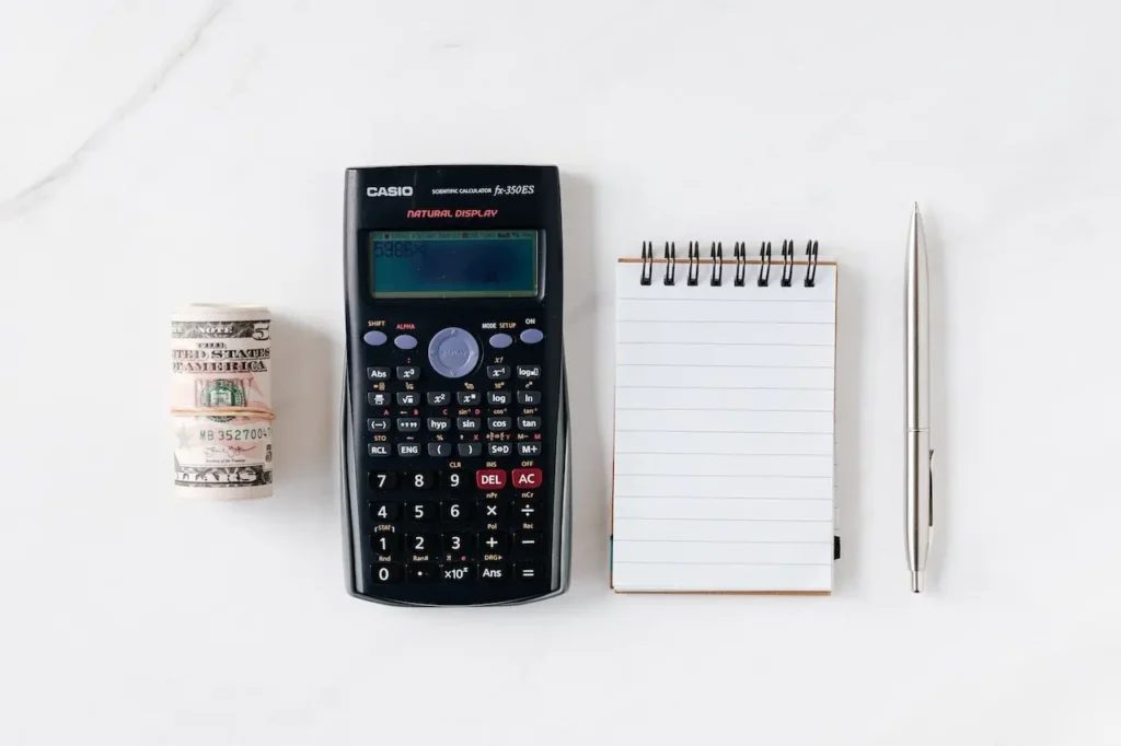 Mesa branca com calculadora, bloco de notas, caneta e dinheiro