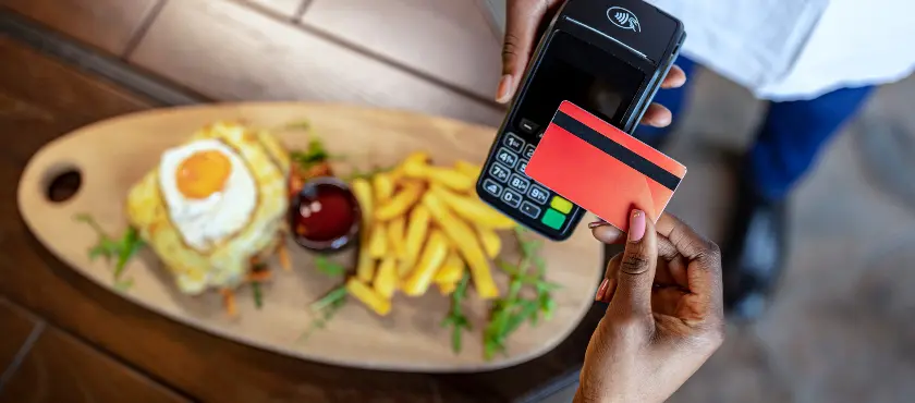 Prato de comida e mão de cliente pagando a conta em maquina de cartão 