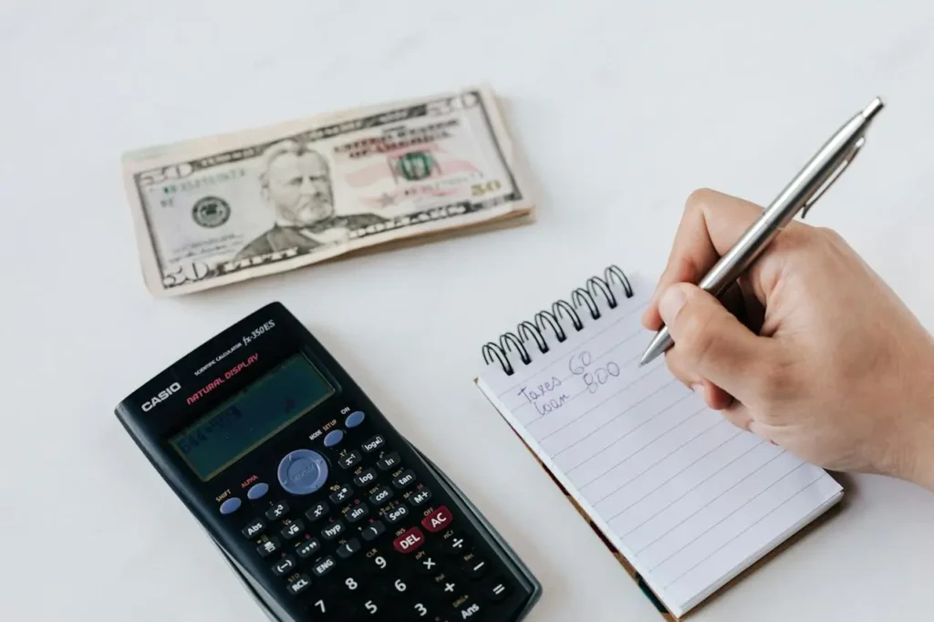 Mesa com bloco de notas, calculadora e dinheiro, mão escrevendo